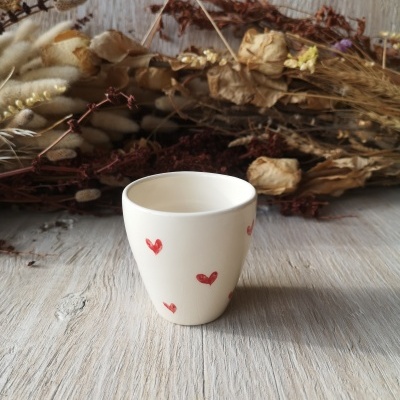 Copo branco com corações vermelhos e flores secas ao fundo