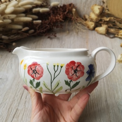 Cremeira branca com flores pintadas, sendo vermelhas, amarelas e uma azul, segurada à mão e fundo de madeira clara