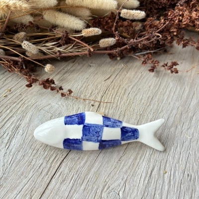 Peixe decorativo de cerâmica azul e branco sobre mesa de madeira com ramos secos