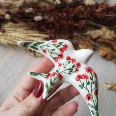 Figura decorativa de cerâmica branca em forma de pássaro com flores vermelhas e folhas verdes