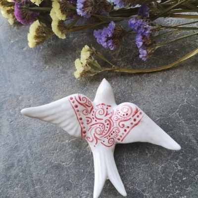 Estatueta de pássaro branca decorada com vermelho junto a flores secas