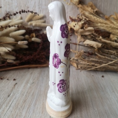 Estátua de porcelana branca com flores roxas sobre base creme