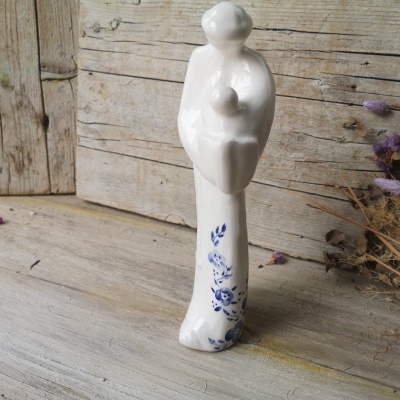 Estátua cerâmica branca com motivos azuis, figura humana e bebé sobre madeira envelhecida