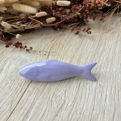 Objeto decorativo lilás em forma de peixe sobre madeira com ramos secos ao lado