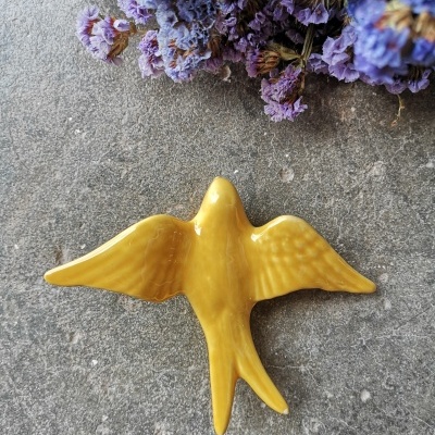 Figura decorativa amarela em forma de pássaro em superfície cinza com flores secas roxas