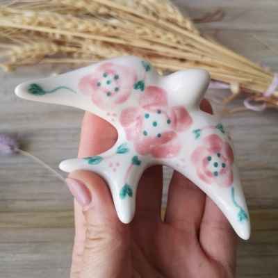 Escultura em cerâmica branca em forma de pássaro com pintura de flores cor-de-rosa e folhas verdes