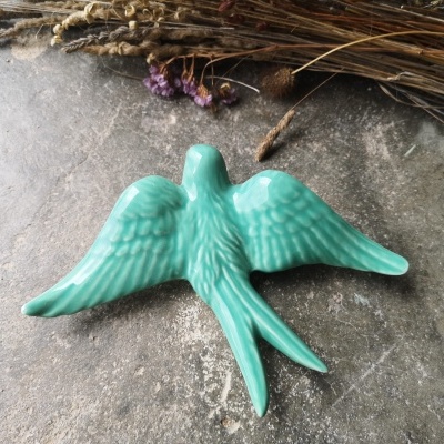 Pássaro decorativo em cerâmica verde com acabamento brilhante sobre superfície de pedra escura.