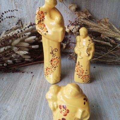 Três estatuetas de cerâmica amarelas decoradas com flores sobre superfície de madeira e ramos secos ao fundo