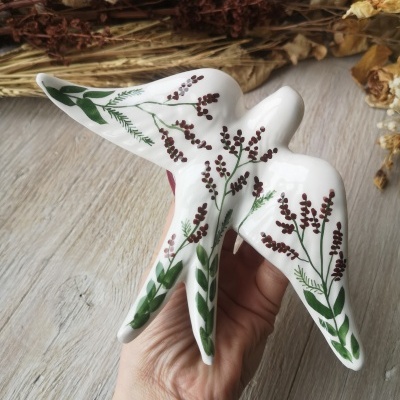 Escultura de pássaro em cerâmica branca com pintura floral em verde e vermelho.