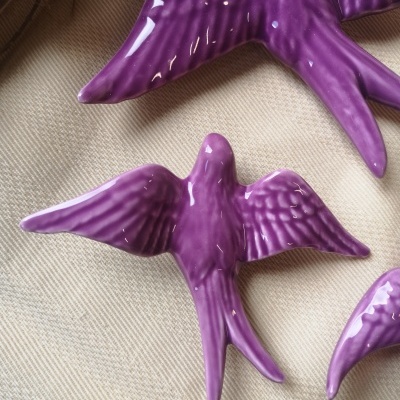 Pássaros decorativos em cerâmica púrpura com textura sobre tecido bege