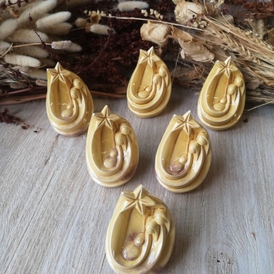 Figuras em cerâmica da Sagrada Família amarelas com estrela, sobre madeira clara e flores secas ao fundo