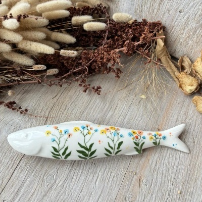Peixe decorativo branco em cerâmica com flores pintadas coloridas e ramos secos ao fundo
