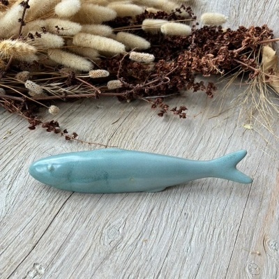 Peixe decorativo cerâmica azul sobre mesa de madeira com ramos secos