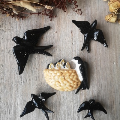 Ornamentos de cerâmica em forma de andorinhas pretas e ninho com ovos sobre madeira clara