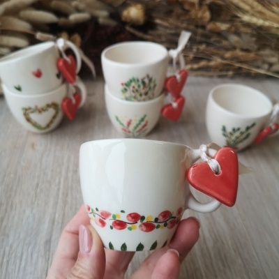 Pequenas chávenas de cerâmica branca com padrões florais e corações vermelhos pendurados