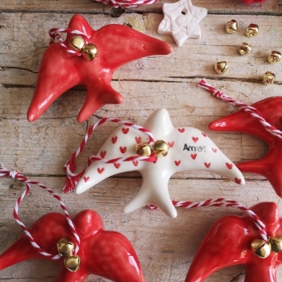 Ornamentos de cerâmica em forma de andorinhas vermelhas e brancas com sinos dourados sobre madeira rústica