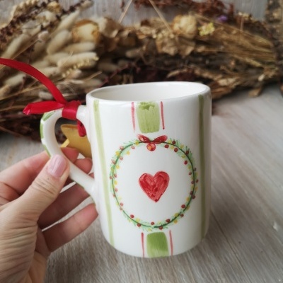 Caneca de cerâmica branca com padrão de riscas verdes e vermelhas e desenho de coração