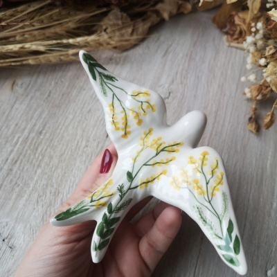 Pássaro decorativo em cerâmica branca com pintura floral amarela e verde.