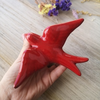 Escultura de pássaro vermelho brilhante em cerâmica sobre mão humana e madeira clara