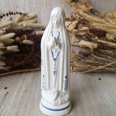 Estátua branca de Nossa Senhora em cerâmica com detalhes azuis e terço azul.