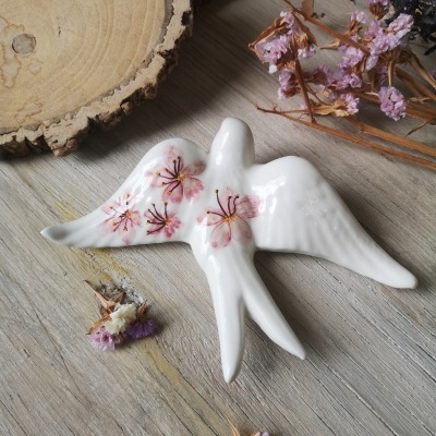 Pombo decorativo em cerâmica branca com flores rosas sobre madeira com flores secas