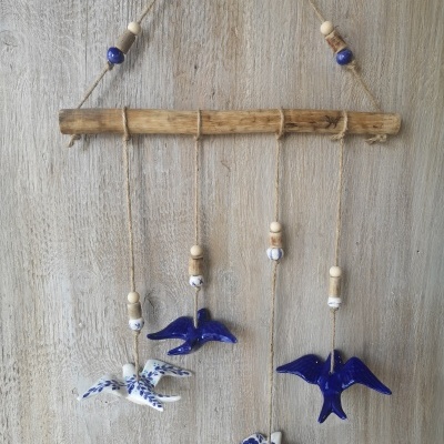 Móbile decorativo com pássaros azuis e brancos pendurado em madeira rústica