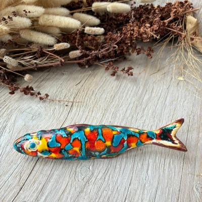 Peixe decorativo em cerâmica colorida sobre madeira com flores secas ao fundo