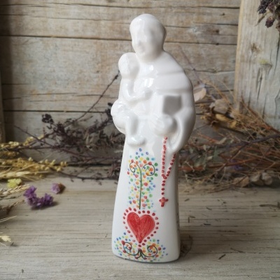 Estatueta cerâmica branca de figura humana com criança e decoração colorida sobre madeira