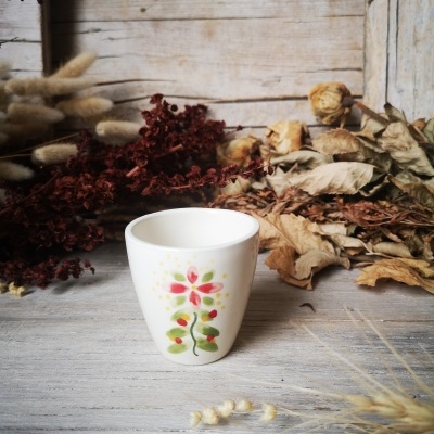 Copo de cerâmica branco com padrão floral colorido sobre mesa de madeira com flores secas.
