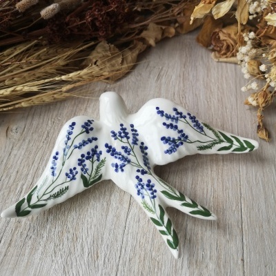 Nicho em cerâmica branca em forma de pássaro com pintura floral azul e verde sobre madeira clara