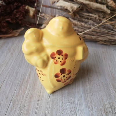 Peça decorativa amarela com flores castanhas e relevo sobre mesa de madeira clara