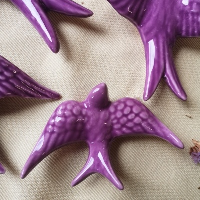 Figuras de pássaros lilás em cerâmica brilhante sobre tecido bege