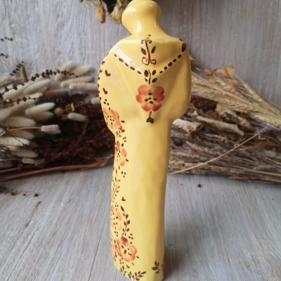 Garrafa cerâmica amarela com pintura floral e ramos secos no fundo