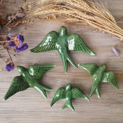 Figuras decorativas de pássaros verdes em cerâmica brilhante com flores secas num fundo de madeira