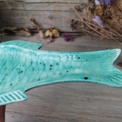 Prato em cerâmica verde formato cauda de peixe sobre mesa de madeira com flores secas