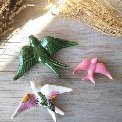 Três pássaros cerâmicos coloridos sobre mesa de madeira com plantas secas