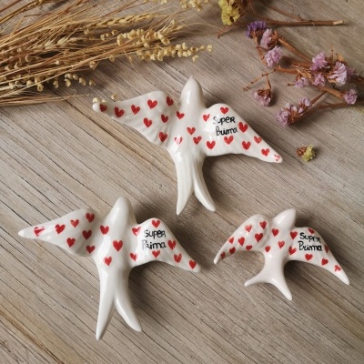 Figuras de cerâmica branca em forma de pássaros decorados com corações vermelhos e texto 'super bruna' sobre madeira clara