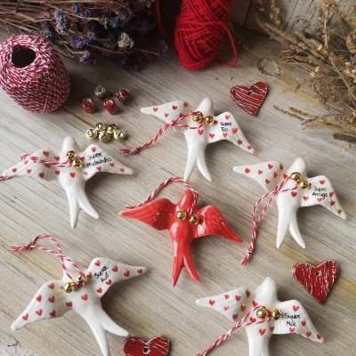 Pendentes de pássaros brancos e vermelhos com sinos dourados e corações vermelhos em fundo de madeira