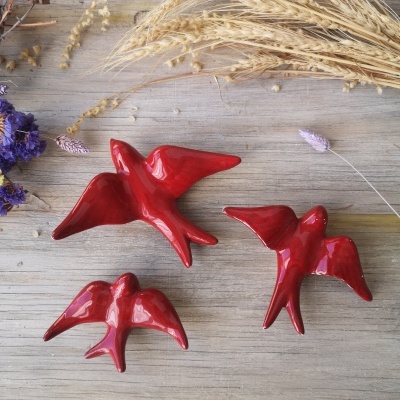 Três pássaros decorativos vermelhos em cerâmica numa superfície de madeira com ramos secos ao redor