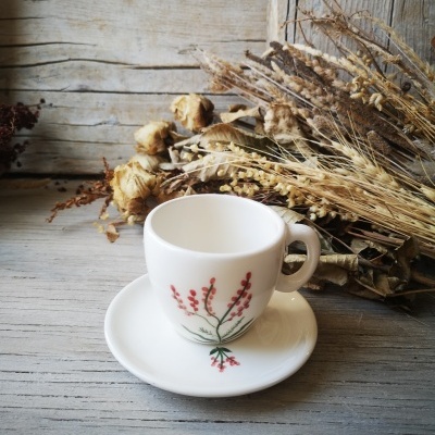 Chávena e pires brancos com padrão floral vermelho e verde junto de flores secas