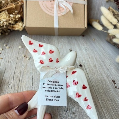Escultura branca em forma de pássaro com corações vermelhos e carta de agradecimento em papel branco com laço bege