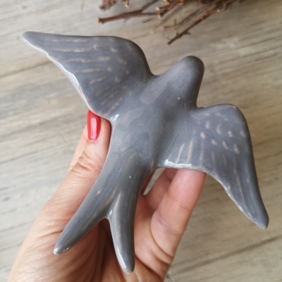 Estatueta cerâmica azul cinzenta em forma de pássaro segurada por mão