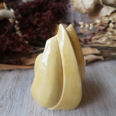 Escultura decorativa em cerâmica amarela com fundo de flores secas