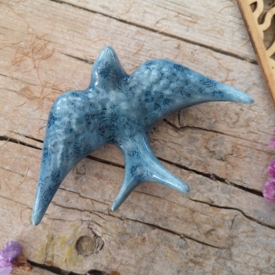 Escultura de pássaro azul em cerâmica sobre madeira com flores roxas