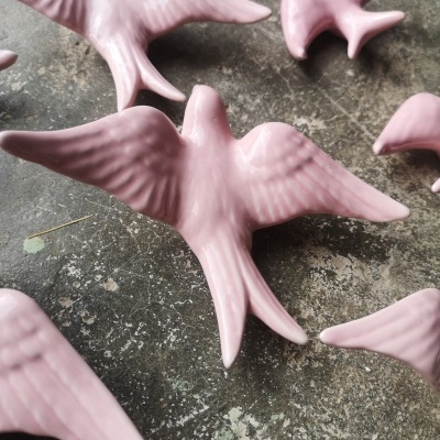 Figuras decorativas de cerâmica cor de rosa em forma de aves sobre superfície cinzenta