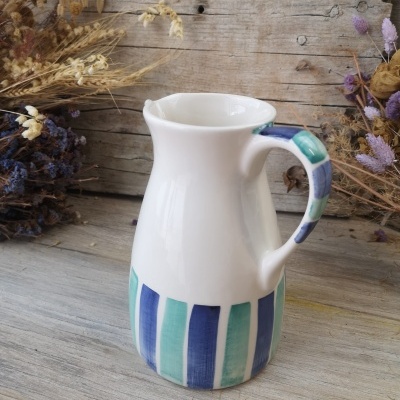 Jarro de cerâmica com riscas azuis e verdes e flores secas ao fundo