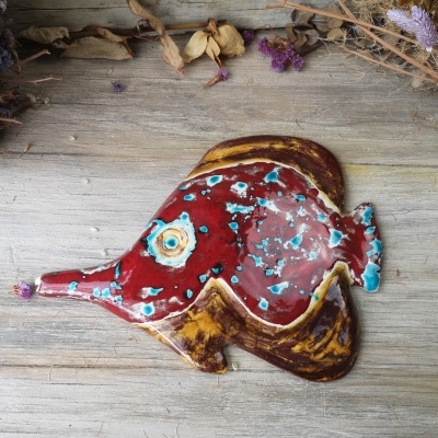 Figura decorativa de peixe em cerâmica colorida sobre madeira clara com flores secas