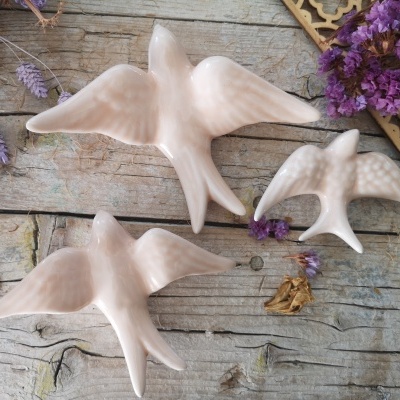 Três pássaros decorativos de cerâmica branca sobre madeira com flores roxas