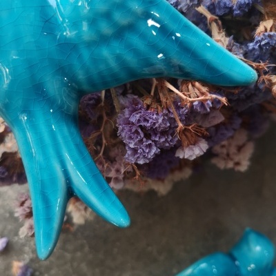 Escultura cerâmica azul de ave com flores secas roxas