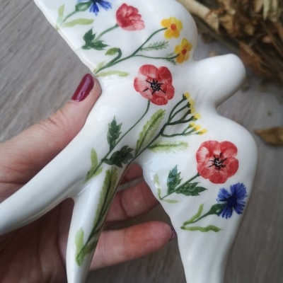 Figura de cerâmica branca em forma de pássaro com pintura de flores coloridas.